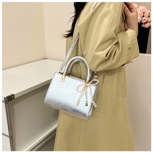 Detail of silver metallic handbag with pearl bow charm on a trench coat background