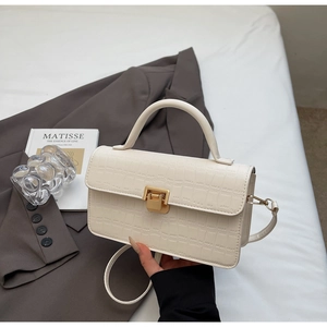 Detail of off-white crocodile texture handbag with gold clasp and top handle grip