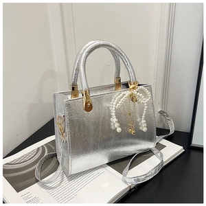 Detail of silver metallic handbag with pearl bow charm and detachable shoulder strap