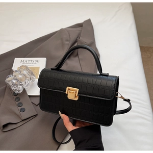 Detail of black crocodile texture bag with golden square lock and round top handle