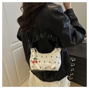 Detail of white pleated shoulder bag with cherry pendant shown on a model in a leather jacket