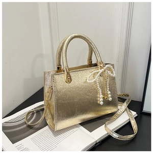 Detail of golden metallic square bag with pearl bow charm on open book display