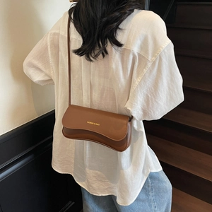 Brown leather baguette shoulder bag with wavy flap and gold text on a minimalist background