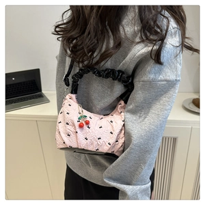 Close-up of pink bow-print shoulder bag featuring a cherry charm and scrunchie handle