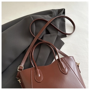 Detailed view of brown leather bucket bag textures on a gray blazer garment