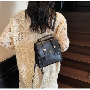 Detail of a vintage black PU leather mini backpack with golden buckles on a model