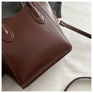 Close-up of deep reddish-brown tote bag with embossed Fashion lettering and gold hardware