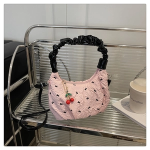 Pink bow-print dumpling bag with cherry charm displayed on a modern metal shelf