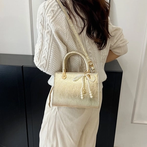 Metallic gold small square bag with pearl bow charm shown as a stylish crossbody hand bag