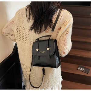 Detail of a chic black leather backpack with a metal dot buckle on a wooden staircase