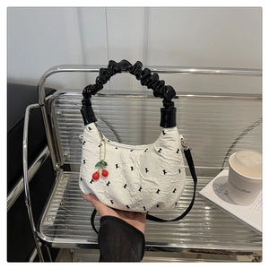 Detail of white textured dumpling bag with black cloud handle and cherry charm accessory