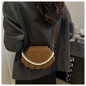 Brown shell-shaped crossbody bag with pearl chain detail and lizard skin texture on model