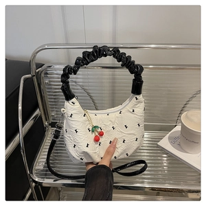 Detail of white wavy textured bag with black K embroidery and cherry charm accessory