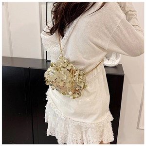 Detail of a gold sequin bucket bag featuring a chain strap and pearl drawstring charm