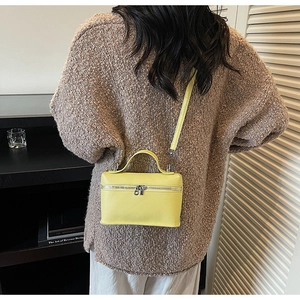 Détail d'un petit sac bandoulière jaune en cuir grainé porté par un mannequin en intérieur