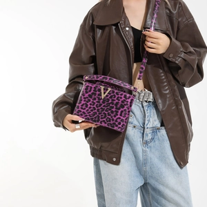 Chic purple leopard print crossbody bag with gold V-buckle worn over a leather jacket