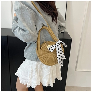 Detailaufnahme der runden Strohtasche mit gepunktetem Band und modischem Outfit