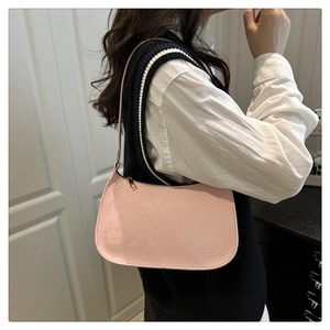 Close-up of pale pink shoulder bag with snake texture pattern shown on a model
