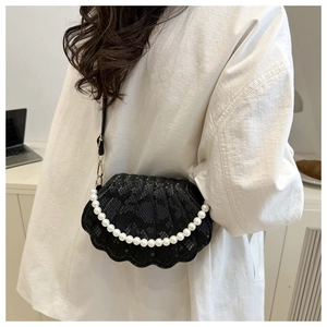 Detail of shell-shaped crossbody bag with pearl accents and snake-skin texture on model
