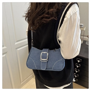 Model wearing dark blue denim crossbody bag with silver buckle and chain strap
