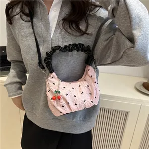 Pink quilted shoulder bag with black bow patterns, cherry charm, and ruffled handle