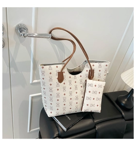 Détail du grand cabas crème et sa pochette avec poignées marron sur une porte blanche