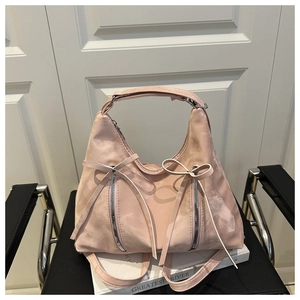 Detail der hellrosa Hobo-Tasche mit dekorativen Schleifen und glänzenden Reißverschlüssen