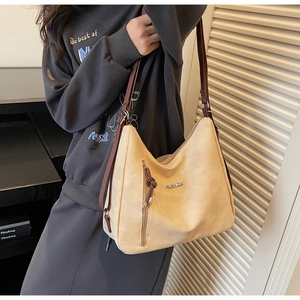 Detail of a large khaki suede tote bag featuring a side zipper pocket and metal fashion logo
