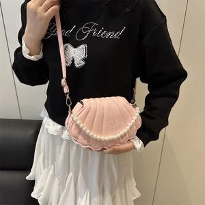 Pink shell-shaped crossbody bag with pearl chain detail worn by a model in a minimalist room