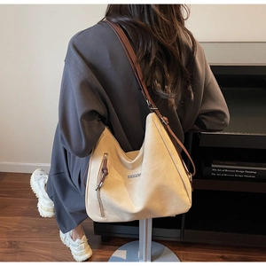 Detailed view of beige suede hobo bag with brown leather strap and metal fashion logo