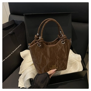 Detail of brown wrinkled patent leather texture and metallic logo on chic bucket bag