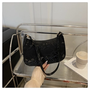 Detail of black snake-embossed shoulder bag with golden hardware and zipper closure