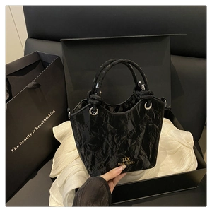 Detail of black crinkle texture handbag with golden logo and twisted rope handle