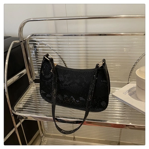 Detail of black faux crocodile skin shoulder bag with gold hardware on a modern cart
