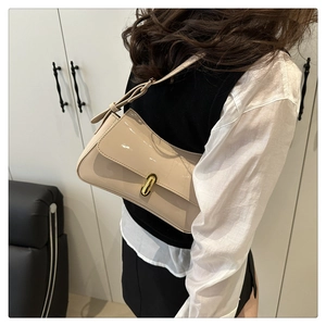 Detail of a beige patent leather saddle bag with gold clasp shown on a model