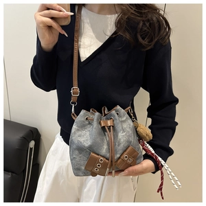 Detail of grey washed denim bucket bag with brown leather drawstring and plush ball charm