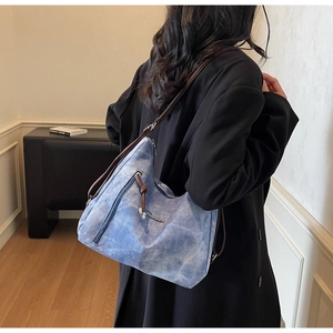 Blue denim tote bag with brown straps shown on shoulder in a minimalist indoor setting