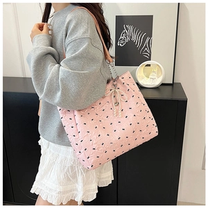 Détail du sac cabas matelassé rose avec motifs de nœuds noirs et pendentif en perle