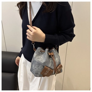 Detail of grey denim bucket bag with brown leather trim and metallic eyelets