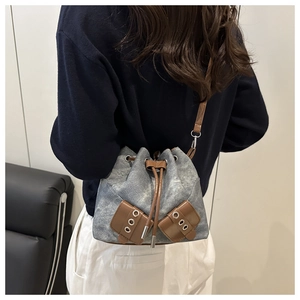Detail of blue denim bucket bag with brown leather drawstring and silver metal eyelets
