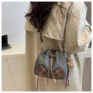 Grey canvas bucket bag with brown leather details and cute bear charm shown on trench coat