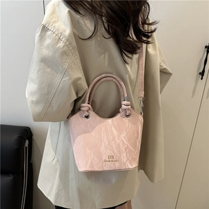 Pink textured bucket bag with circular handles and shoulder strap worn by a model