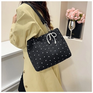 Détail du sac cabas noir à motifs nœuds blancs, bandoulière chaîne et breloque perle