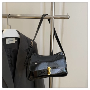 Detail of black patent leather baguette bag featuring a gold capsule-shaped lock closure