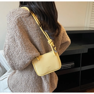 Detail view of yellow leather crossbody bag featuring knot strap and embossed logo