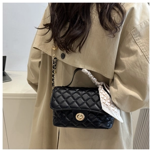 Detail of black quilted handbag with golden twist lock and silk scarf wrapped handle