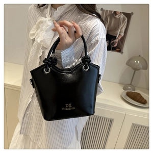 Detail of black matte bucket bag with knot handles and gold logo in home setting