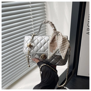 Detail of silver quilted handbag featuring a scarf-wrapped handle and metal ball charm
