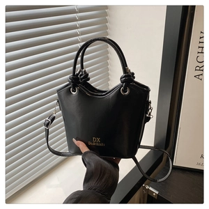 Detail of black glossy bucket bag featuring knot handles and silver metal hardware