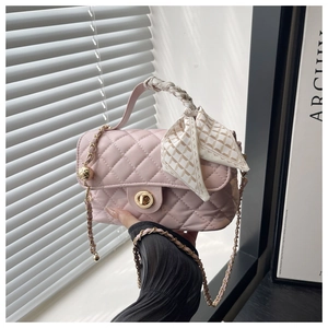 Close-up of pink quilted crossbody bag with golden turn-lock and silk scarf on handle